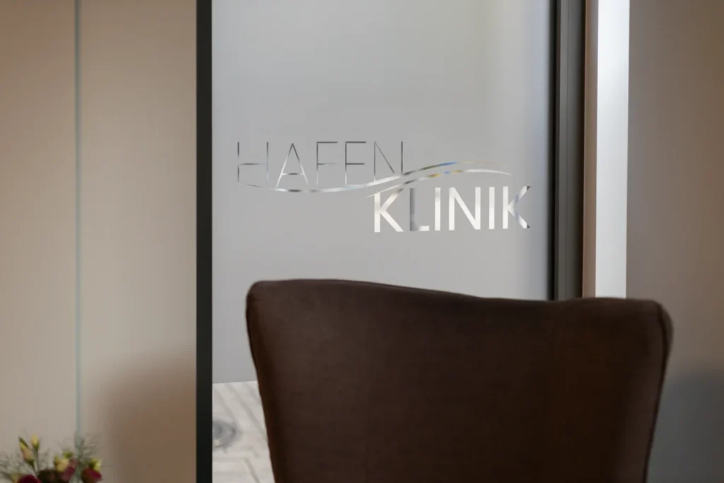 Milchglastür mit Hafenklinik-Schriftzug und Sessel im Wartebereich